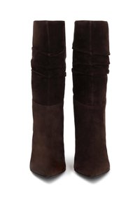 Botas de ante marrón hasta la rodilla con un diseño holgado, que presentan una punta afilada y una textura suave. Los detalles incluyen suaves pliegues a lo largo del eje.