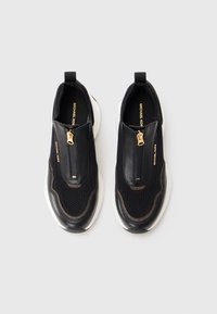 Sorte slip-on sneakers med mesh overdel, læderdetaljer, guld lynlås og hvid sål. Har en afrundet tå og trækflapper.