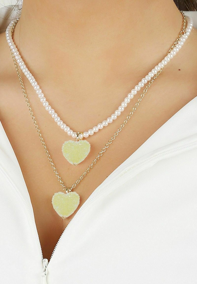 Lagerade halsband med vita pärlor och guldkedjor, med två hjärtformade hängande smycken i ljusgul och genomskinlig finish.