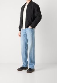 Chaqueta bomber negra, camiseta blanca, jeans de color azul claro y zapatillas oscuras. Atuendo informal con un corte relajado y un diseño simple.