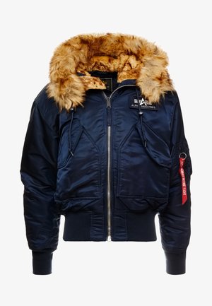 Giubbotto bomber navy con colletto in ecopelliccia, chiusura con zip, polsini e orlo a coste, due tasche frontali e un'etichetta rossa con testo sulla manica sinistra.