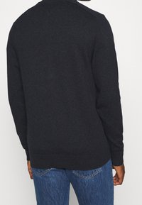 Donkerblauwe trui, gebreide textuur, een ronde hals, lange mouwen, geribbelde manchetten en zoom, gedragen met een blauwe spijkerbroek, achterkant zichtbaar.