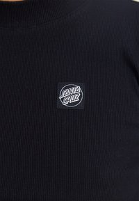 Svart ribbestrikket langermet skjorte med et kvadratisk merke med hvit "Santa Cruz"-logo i midten. Glatt tekstur og høy halsdesign.