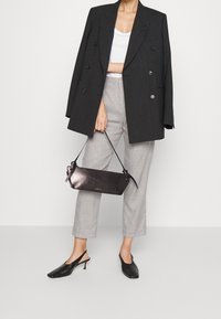 Svart dubbelknäppt kavaj, vit kort topp, ljusgrå byxor, svarta slingback skor och liten svart läderväska med Rem.