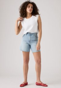 Witte mouwloze top, lichtblauwe denim shorts, rode mesh balletschoenen. De outfit heeft een losse pasvorm en een casual stijl zonder patronen.