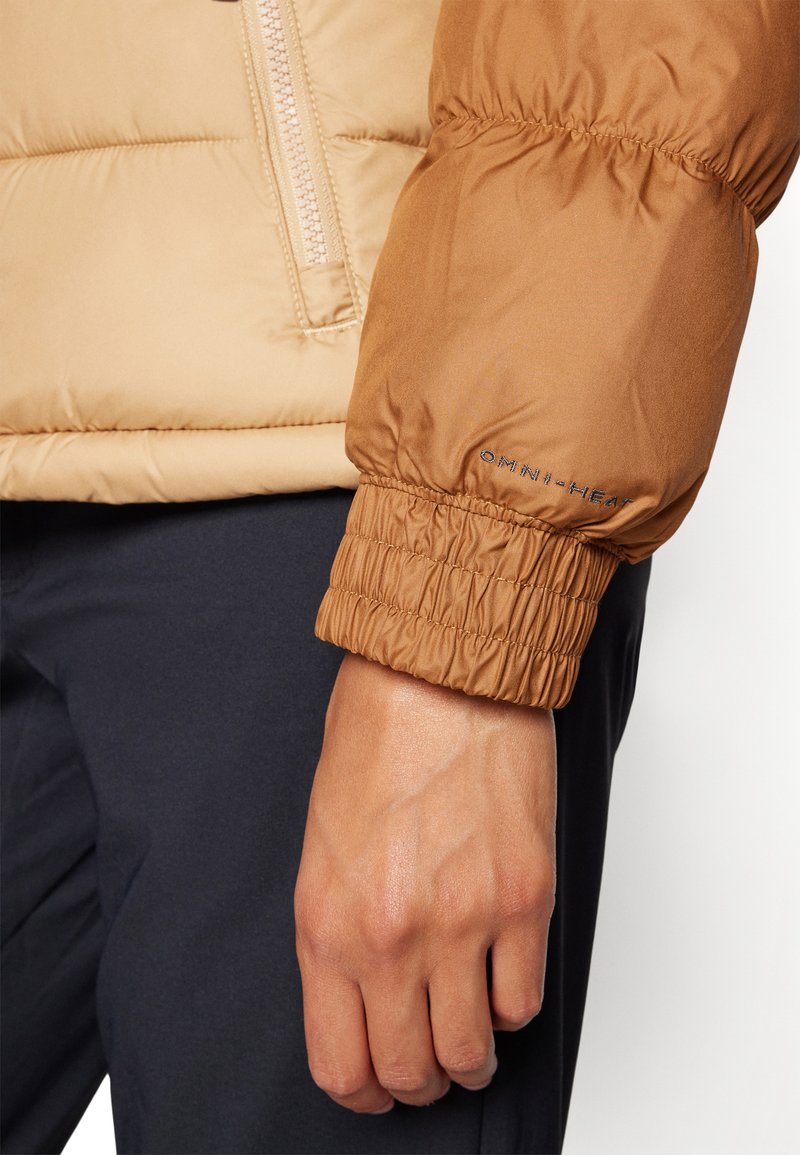 Beżowa ocieplana kurtka o błyszczącej wykończeniu, z zamkiem błyskawicznym i elastycznymi mankietami. Na mankiecie widoczne jest logo "OMNI-HEAT".