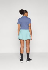 Polo de color navy combinado con una falda skater de azul claro, calcetas negras hasta la rodilla y zapatillas deportivas negras. Tejido suave, diseño informal.