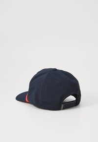 Casquette de baseball marine avec visière courbée, fermeture ajustable à l'arrière et accent rouge sur le côté. Le tissu est lisse et durable.