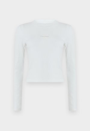 Haut court blanc à manches longues en maille côtelée, avec col rond et petit logo Calvin Klein centré sur la poitrine.