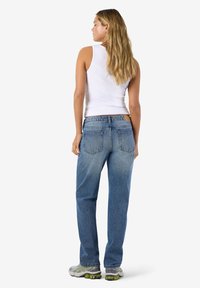 Ανοιχτό μπλε τζιν με χαλαρή εφαρμογή, που διαθέτει ξεθωριασμένες περιοχές και δύο πίσω τσέπες, συνδυασμένα με λευκό τοπ και αθλητικά παπούτσια.