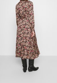 Abito midi stampato floreale marrone con maniche lunghe, vita cintrata, gonna fluida e stivaletti neri con cuciture decorative.