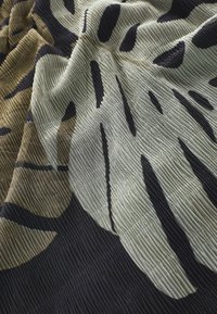 Tissu texturé présentant de grandes feuilles abstraites dans une palette de couleurs beige, vert olive et noir, avec une texture côtelée visible.