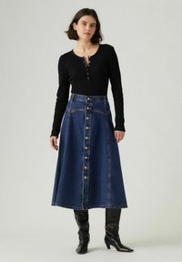 Czarny prążkowany top z długimi rękawami zestawiony z ciemnoniebieską spódnicą midi z wysokim stanem i guzikami. Modelka ma na sobie czarne kozaki do kolan.