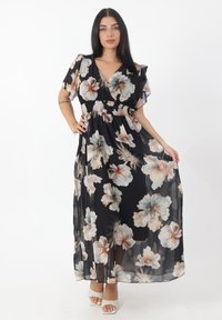 Robe maxi noire à motifs floraux avec des manches courtes, présentant une taille cintrée et un tissu léger et transparent orné de grandes fleurs pastel.