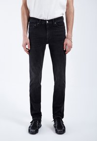 Jeans de mezclilla negra con un corte ajustado, que presentan un diseño clásico de cinco bolsillos, costuras sutiles y un cierre estándar de botón y cremallera.