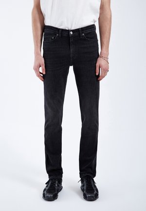 Jeans de mezclilla negra con un corte ajustado, que presentan un diseño clásico de cinco bolsillos, costuras sutiles y un cierre estándar de botón y cremallera.