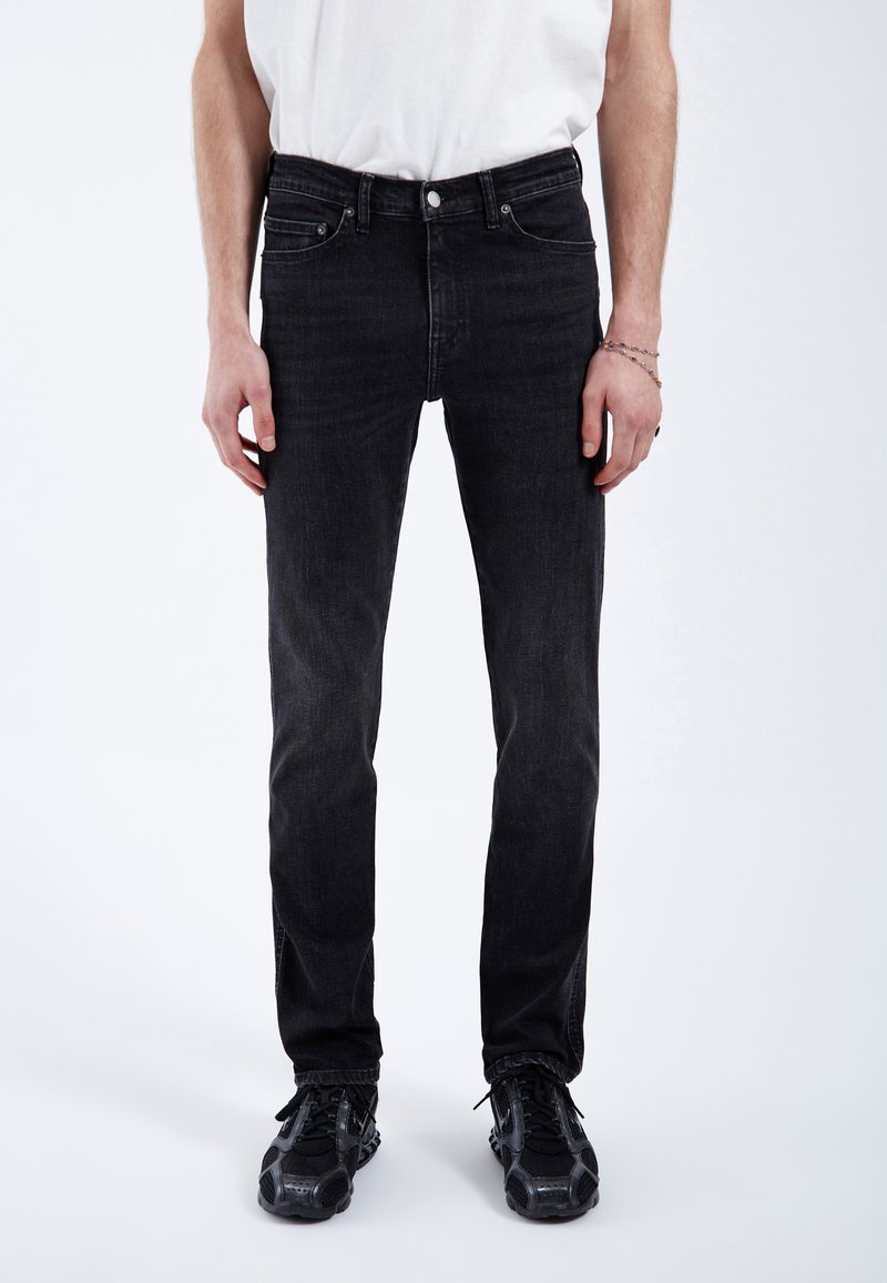 Jeans de mezclilla negra con un corte ajustado, que presentan un diseño clásico de cinco bolsillos, costuras sutiles y un cierre estándar de botón y cremallera.