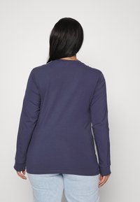 Námořnické tričko s dlouhým rukávem z měkké tkaniny s kulatým výstřihem, se rovnými lemy a přiléhavými rukávy, nošené s světle modrými džíny.