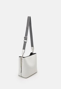 Witte leren schoudertas met een gestructureerde afwerking, zwarte binnenkant en een zwart-witte strap met patroon, bevestigd met zilveren hardware.