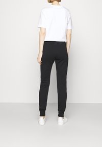 Black joggers with a fitted design, paired with a white short-sleeve t-shirt. Material appears soft, with elastic ankle cuffs and side seams visible.