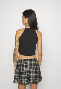 Black cropped halter top with a scalloped hem paired with a pleated plaid mini skirt in black, white, and brown tones.