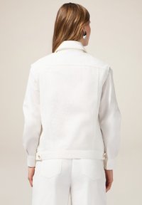 Witte spijkerjas met textuur op de schouders, knoopverwisting en een getailleerde pasvorm. Voorzien van achterzakken en een minimalistisch ontwerp.