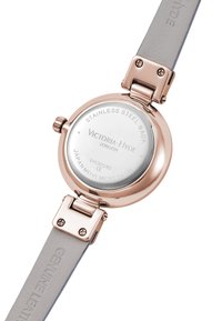 Montre ronde avec un fond en acier inoxydable, un boîtier en or rose et un bracelet en cuir véritable gris. Présente un système de charnière et des détails sur le bracelet.