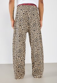 Leopardmønster bredbeinte bukser i beige med svart mønster. Har en rød elastisk midje. Mykt, lett stoff med en avslappet passform.