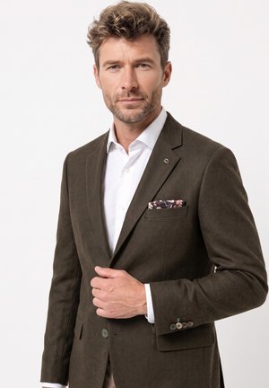 Man with short curly hair wearing a dark brown blazer, white shirt, and floral pocket square, looking directly ahead.