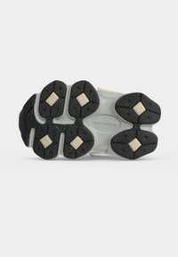 Σόλα παπουτσιού New Balance με μαύρα ελαστικά πέλματα πρόσφυσης και μπεζ ενθέματα μαξιλαριού σε σχήμα ρόμβου σε λευκό φόντο.