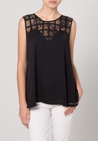 Schwarzes ärmelloses Oberteil mit transparentem Spitzenbesatz mit geometrischen Mustern am Ausschnitt und einer lockeren, fließenden Silhouette.