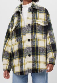 Rutig jacka i mjukt, texturerat tyg med nyanser av svart, vitt, gult och grönt. Knapplåsning och två bröstfickor. Avslappnad passform.