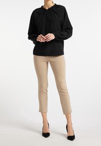 Blouse noire à manches longues avec un col froncé, associée à un pantalon beige ajusté et des escarpins noirs. Tissu lisse, coupe décontractée, détails minimaux.