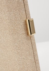 Kabelka se zlatým třpytem, která má texturovaný povrch, magnetické zapínání s obdélníkovým zlatým detailem a elegantní, úhlový design.