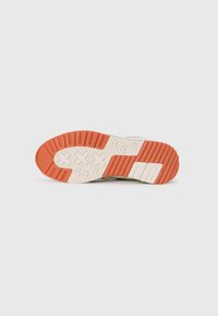 Sneaker sole in light beige and orange, featuring a textured tread pattern with grooves for traction and cushioning.