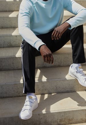 Lichtblauwe sweater met ronde halslijn, zwarte broek met witte zijstrepen, en witte sneakers met klittenbandsluitingen.