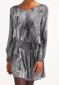 Dlouhé šaty s černobílým pruhovaným vzorem. Mají gumičkový pas a volný střih, s výstřihem do V a splývavou texturou.