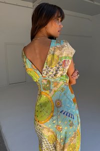 A színes ruha térképnyomattal, rövid ujjakkal és mély V-hátrészes dizájnnal rendelkezik. Könnyű anyagból készült, részletes mintákkal és díszítésekkel.