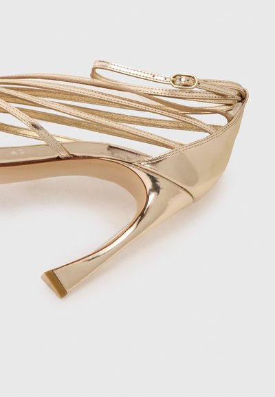 Gold metallic high-heeled shoe with multiple narrow straps, pointed toe, and a sleek stiletto heel, featuring a subtle matte texture.