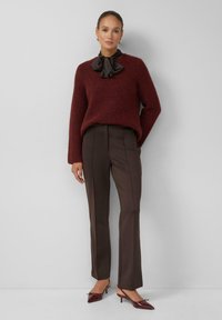 Burgundowa sweter z dzianiny z falbaniastym dekoltem, w zestawieniu z brązowymi spodniami o dopasowanym kroju. Całość uzupełniają burgundowe czółenka ze szpiczastym noskiem.