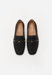 Mocassini neri realizzati in morbido suede con borchie dorate e una cintura decorativa con bottoni neri e dorati. Suola piatta e design a punta arrotondata.