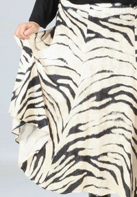 Cream skirt with black zebra stripes, flowing design, lightweight fabric, and layered hem that creates movement. Hand visible at the waist.