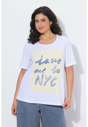 Kvinde med krøllet mørkt hår iført øreringe, hvid t-shirt med gule striber og teksten "take me to NYC", samt blå jeans.