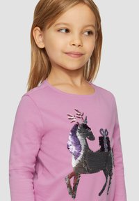 Rosa Langarmhemd mit einem glänzenden, pailettenbesetzten Rentierdesign, das Geweih und ein Geschenk zeigt. Glatte Textur mit rundem Ausschnitt und figurbetontem Schnitt.