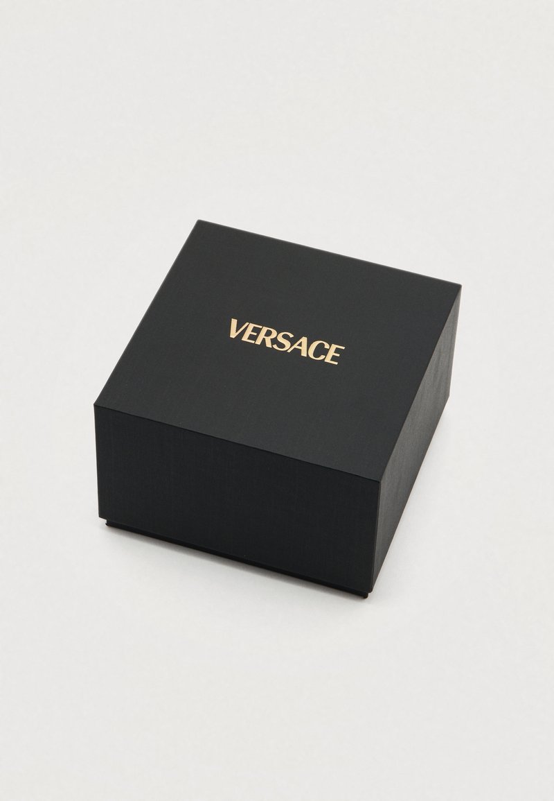 Schwarze quadratische Schachtel mit matter Oberfläche und einem goldenen "VERSACE"-Logo auf der Oberseite. Minimalistisches Design mit geraden Kanten.
