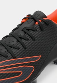Black soccer cleat with textured upper, orange accents, and black laces. Features hexagonal pattern and a sleek, streamlined shape.