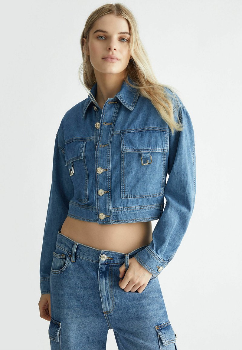 Giacca di jeans cropped di un azzurro chiaro con bottoni dorati, due tasche frontali e colletto classico. Tessuto testurizzato, design aderente.