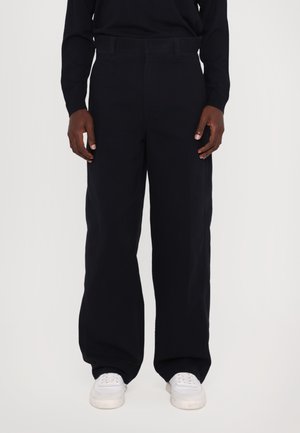 Black wide-leg trousers made from cotton, featuring a high waist, flat front, and side pockets. Paired with white sneakers.