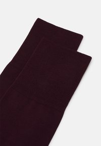 Medias hasta la rodilla en borgoña con un tejido texturizado en la parte superior y una sección inferior suave. El diseño incluye acentos acanalados y un acabado suave.