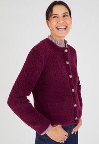 Cardigan fuzzy bordeaux con scollo rotondo, cinque bottoni dorati sul davanti e una tasca applicata sul lato sinistro.